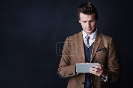 Photo for Success is only a tap away. Studio shot of a young businessman using his tablet against a dark background - Royalty Free Image