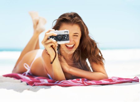 Photo for Great shot. Full length portrait of a gorgeous young woman taking a picture with a camera while lying down at the beach - Royalty Free Image