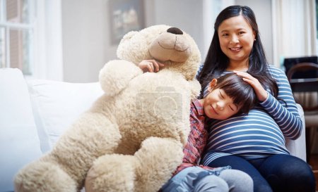 Photo for Our family is growing. Cropped portrait of a little girl sitting with her mother and her teddybear on the sofa - Royalty Free Image
