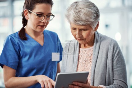 Foto de Así que todos sus registros médicos están aquí. una joven enfermera y su paciente mayor mirando una tableta en el hogar de ancianos - Imagen libre de derechos