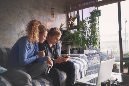 Foto de Los mejores socios son los mejores amigos. una pareja joven usando un teléfono inteligente mientras juega juegos de ordenador en el sofá en casa - Imagen libre de derechos