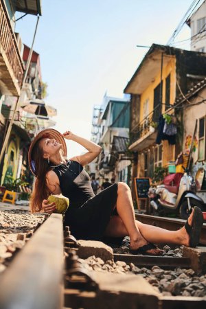 Foto de Esta ciudad electrificará todos tus sentidos. una mujer tomando agua de coco mientras se relaja en las vías del tren en las calles de Vietnam - Imagen libre de derechos