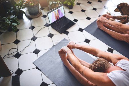 Foto de Otro día otro nuevo video de yoga. dos hombres usando un ordenador portátil mientras pasan por una rutina de yoga en casa - Imagen libre de derechos