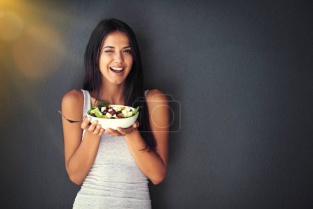 Téléchargez les photos : Femme clin d'oeil avec salade, alimentation saine et nutrition, portrait et légumes isolés sur fond de mur. Heureux, le corps et la santé avec le bien-être, l'alimentation et le modèle féminin pour perdre du poids avec l'espace de maquette. - en image libre de droit