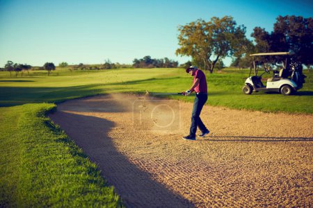 Photo for Safely out of the sand trap. a young man hitting the ball out of the bunker during a round of golf - Royalty Free Image