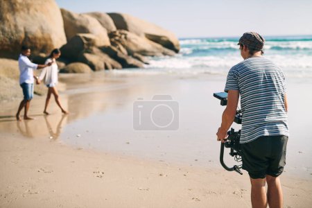 Photo for Capturing special moments. Rearview shot of a focused young man shooting a scene with a state of the art video camera outside on a beach during the day - Royalty Free Image