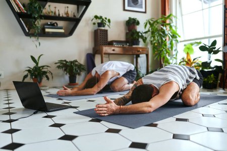 Photo for Let it go. two men using a laptop while going through a yoga routine at home - Royalty Free Image