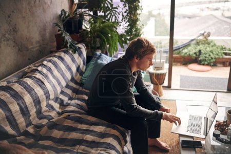 Photo for As long as Im staying home, Im staying connected. a young man using a laptop on the sofa at home - Royalty Free Image