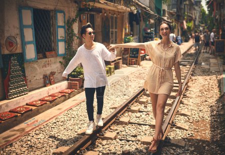 Téléchargez les photos : Trouvez quelqu'un qui corresponde à votre spontanéité. un jeune couple marchant sur les voies ferrées à travers les rues du Vietnam - en image libre de droit