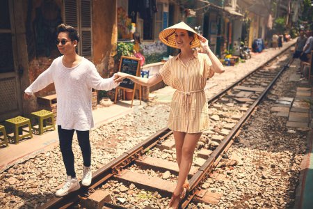 Foto de Haz algo todos los días que haga feliz a tu corazón. una joven pareja caminando en las vías del tren a través de las calles de Vietnam - Imagen libre de derechos