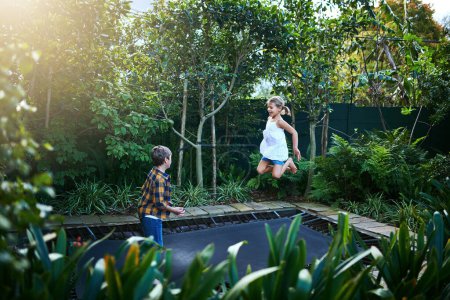 Téléchargez les photos : Jouer ensemble nous apporte tant de joie. un adorable petit garçon et une petite fille sautant sur un trampoline dans la cour arrière à la maison - en image libre de droit