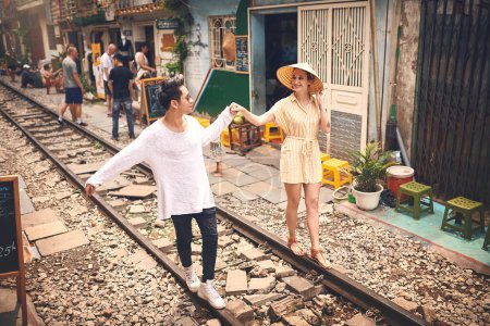 Téléchargez les photos : Première règle de voyage Trouvez le véritable amour. un jeune couple marchant sur les voies ferrées à travers les rues du Vietnam - en image libre de droit