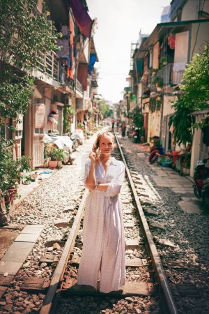 Foto de Cada ciudad que visito se convierte en parte de mí. una joven caminando en las vías del tren por las calles de Vietnam - Imagen libre de derechos