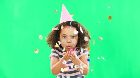 Little girl, birthday and blowing confetti on green screen for party celebration isolated against a studio background. Portrait of cute kid celebrating event with glitter decor for new year on mockup.