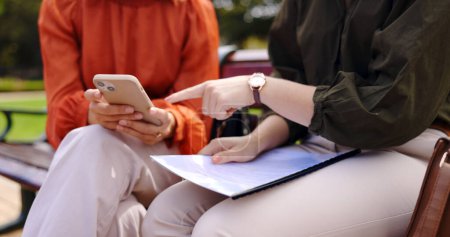 Photo for Business, closeup and women on a bench, smartphone or planning for collaboration, documents or discussion. Female professionals, freelancers or partners in a park, cellphone or mobile app for project. - Royalty Free Image