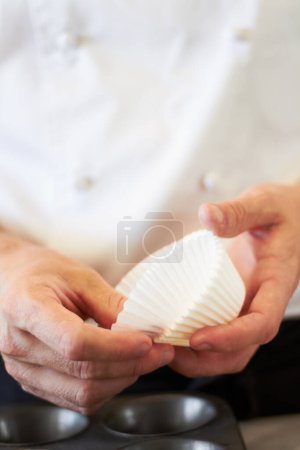 Photo for Cupcake, person hands and baking in a kitchen with muffin wrapper and cooking in a bakery. Prepare, paper cup and food with chef in a restaurant, coffee shop or cafe with sweet cake and pastry. - Royalty Free Image