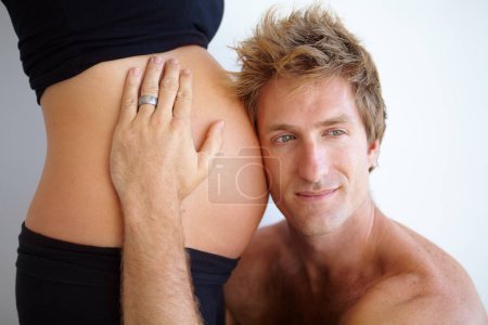 Photo for Man listening with head on stomach, pregnant woman and excited new parents in studio on white background. Love, support and pregnancy, mother and father with hand on belly and future baby in family - Royalty Free Image