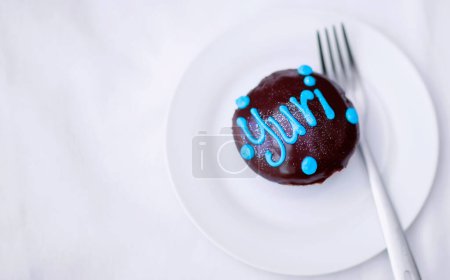 Téléchargez les photos : Cupcake, gâteau au chocolat et dessert sur une assiette pour une fête d'anniversaire avec un nom ou un travail. Nourriture, mauvaise alimentation et sucre de boulangerie sur une table pour célébrer lors d'une fête pour Yuri d'en haut. - en image libre de droit