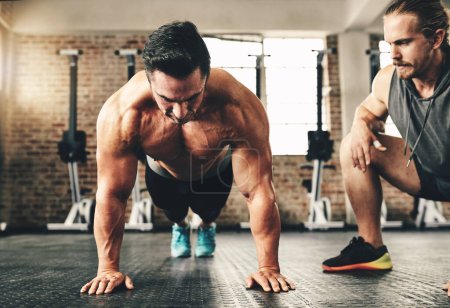 Push up, strong and man or personal trainer in gym support, motivation and helping body builder in training. Muscle, fitness and focus of people exercise or workout on floor, advice or accountability.