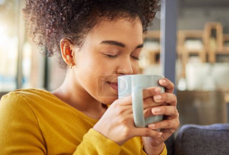 Foto de Mujer africana, taza de café y olor en el sofá, sabor y energía para comenzar la mañana en el apartamento. Chica, feliz y beber para relajarse con té, matcha o espresso con fragancia, pensando y taza en casa. - Imagen libre de derechos
