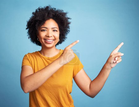 Photo for Happy, portrait of woman pointing and against blue background for product placement. Direction or marketing, advertising or giveaway and female person pose with hand gesture in studio backdrop. - Royalty Free Image