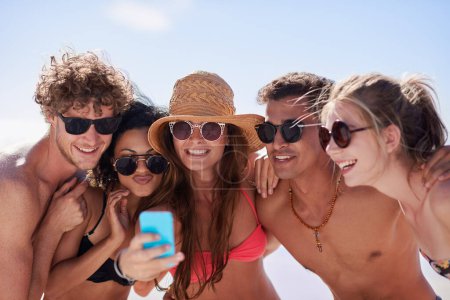 Foto de Redes sociales, verano y amigos en la playa con un teléfono para publicar una actualización de estado mientras están de vacaciones juntos. Móvil, libertad y un grupo de jóvenes al aire libre en la naturaleza para viajes de vacaciones. - Imagen libre de derechos