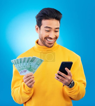 Photo for Man, phone and money in studio with prize, esports gambling or happy for success by blue background. Young asian guy, student and smartphone with cash, fintech or crypto with profit, bonus or goals. - Royalty Free Image