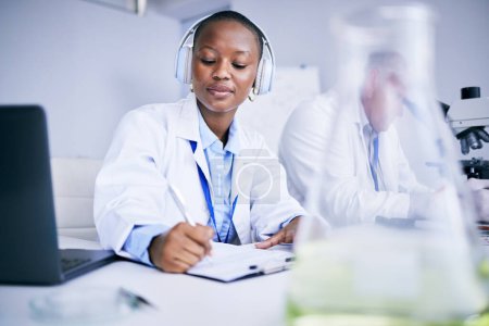 Téléchargez les photos : Des notes de recherche, de la musique et une femme noire dans un laboratoire étudiant les soins de santé et rédigeant un rapport. Innovation, éducation et un scientifique africain avec un casque pour un podcast tout en faisant de la paperasse médicale. - en image libre de droit