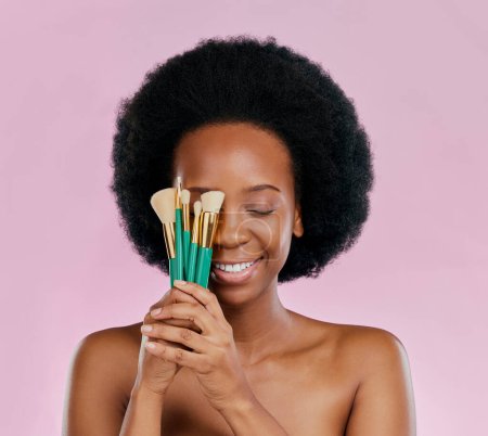 Photo for Face, makeup and black woman with brushes, eyes closed and smile in studio isolated on a pink background. Skincare, facial cosmetics and African model with tools for foundation, powder and beauty - Royalty Free Image