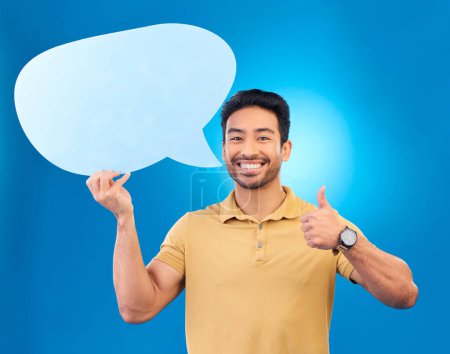 Photo for Young man, speech bubble and studio portrait for thumbs up, opinion and social network by blue background. Indian guy, student or model for yes icon, mock up space and cardboard sign for promotion. - Royalty Free Image