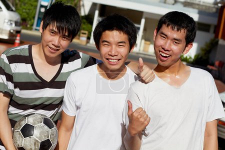 Téléchargez les photos : Hommes asiatiques, amis et portrait avec ballon de football, pouces levés et sourire au campus ensemble pour le sport en plein air. Étudiants japonais heureux, groupe et icône oui avec football pour l'entraînement, l'exercice ou les jeux. - en image libre de droit