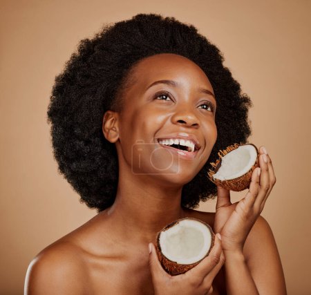 Photo for Beauty, skincare and coconut with a model black woman in studio on a brown background for natural treatment. Thinking, skin and cosmetics with a happy young female person holding fruit for oil. - Royalty Free Image
