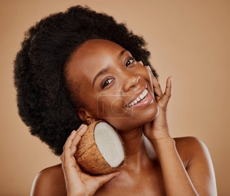 Photo for Portrait, skincare and coconut with a model black woman in studio on a brown background for natural treatment. Beauty, skin and cosmetics with a happy young female person holding fruit for oil. - Royalty Free Image