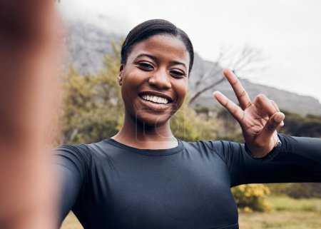 Téléchargez les photos : Fitness, femme noire et prise de selfie en forêt pour l'entraînement avec signe de paix. Entraînement ou exercice, santé bien-être ou motivation et athlète féminine heureuse avec emoji main pour les médias sociaux dans les bois. - en image libre de droit