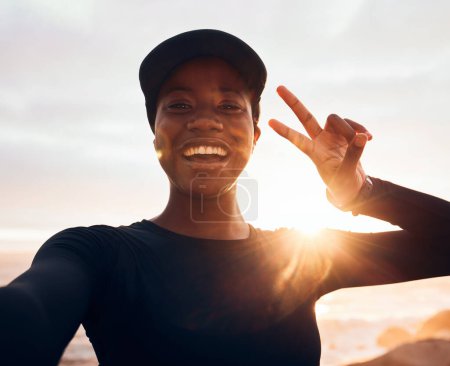 Foto de Selfie, fitness y retrato de mujer al amanecer en la naturaleza para hacer ejercicio, maratón de entrenamiento y correr. Deportes, maqueta y mujer africana con signo de paz para el calentamiento, el entrenamiento y el bienestar. - Imagen libre de derechos