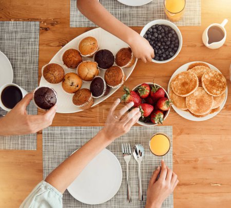 Photo for Breakfast, food and hungry people in dining room, eating healthy and above table setting or home in the morning. Fruit, pancakes and hands on strawberry or muffin plate for nutrition or diet. - Royalty Free Image