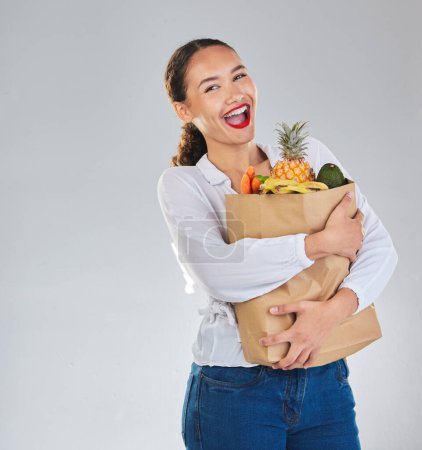 Photo for Excited, portrait and woman grocery shopping for fruit on mockup space in studio isolated on a white background. Bag, food or customer with vegetables for nutrition, healthy diet and supermarket deal. - Royalty Free Image