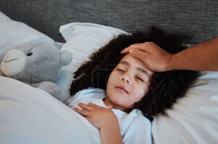 Foto de Enfermo, fiebre y niño durmiendo en la cama para descansar para recuperarse de la gripe, el resfriado o las alergias en su casa. Enfermedad, cansancio y mano de padre comprobando la temperatura de su hija en su habitación en su casa - Imagen libre de derechos