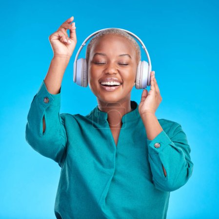 African woman, headphones and studio for dancing, music or listen with smile by blue background. Young gen z student, sound tech and happy for audio streaming subscription, radio or excited for dance.