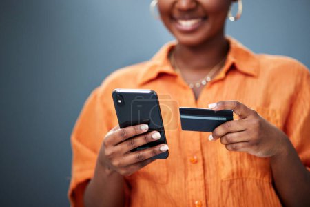Foto de Mujer africana, tarjeta de crédito y teléfono en estudio con comercio electrónico, pago digital o sonrisa de fondo. Chica, smartphone y fintech con compras en línea, facturas y ciberseguridad con contraseña para escribir. - Imagen libre de derechos