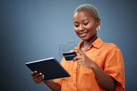 Téléchargez les photos : Femme africaine, carte de crédit et tablette en studio pour le commerce électronique, paiement numérique ou sourire en arrière-plan. Fille, écran tactile et fintech avec achats en ligne, factures ou cybersécurité avec mot de passe de saisie. - en image libre de droit