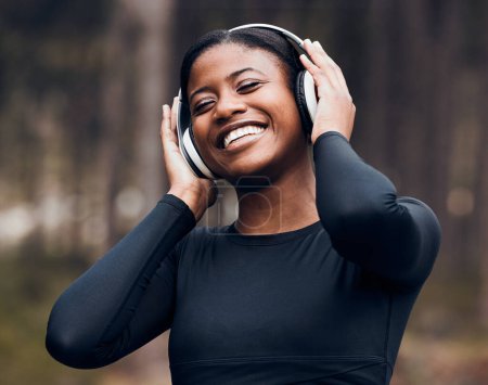 Foto de Fitness, mujer negra escuchando música y en maderas con auriculares felices por el entrenamiento. Ejercicio o entrenamiento, entrenamiento o atleta feliz y femenina escuchar radio o podcast para la motivación en la naturaleza. - Imagen libre de derechos