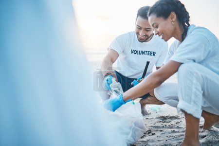 Téléchargez les photos : Volontaire, maquettes et personnes nettoyant la plage pour la journée mondiale de la terre, soins et gentillesse pour l'environnement naturel. Aider, recycler et heureux homme et femme ramasser les déchets plastiques et la pollution sur le sable de l'océan - en image libre de droit