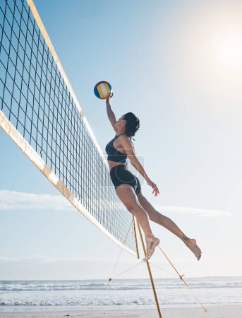 Photo for Woman, jump and volleyball in air on beach by net in serious sports match, game or competition. Fit, active and sporty female person jumping or reaching for ball in volley or spike by the ocean coast. - Royalty Free Image