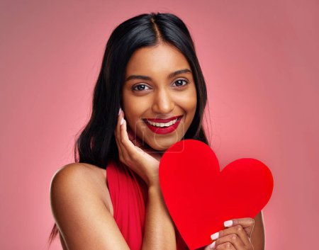 Photo for Portrait, heart and romance with a woman on a pink background in studio for love or affection. Smile, emoji and social media with a happy young female holding a shape or symbol on valentines day. - Royalty Free Image