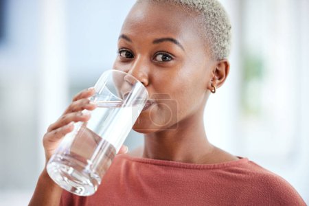 Foto de Salud, vidrio y retrato de una mujer bebiendo agua para hidratación, bienestar y dieta líquida. Saludable, h2o y foto de una joven africana disfrutando de una bebida fría o bebida en su casa - Imagen libre de derechos