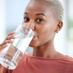 Health, glass and portrait of a woman drinking water for hydration, wellness and liquid diet. Healthy, h2o and headshot of young African female person enjoying a cold beverage or drink at her home