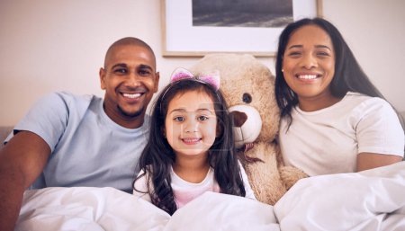 Photo for Family, morning and happy portrait on a bed at home with a smile, teddy bear and comfort for quality time. Man, woman or parents and a girl kid together in the bedroom for bonding with love and care. - Royalty Free Image