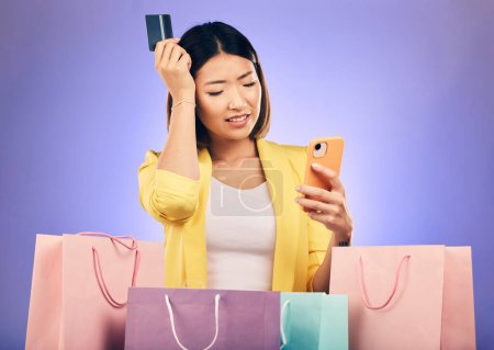 Photo for Woman, confused and credit card, phone and online shopping scam, news or fintech payment problem. Stress, retail bag and sad asian person in e commerce mistake on mobile and purple studio background. - Royalty Free Image