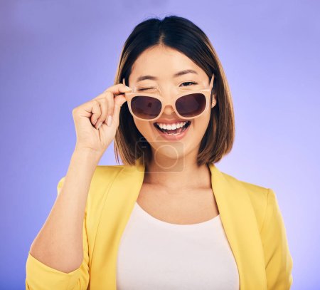 Photo for Happy, portrait of asian woman wink with glasses in studio, purple background and fashion. Face, female model and blink emoji with sunglasses for secret, fun personality and gen z girl in good mood. - Royalty Free Image